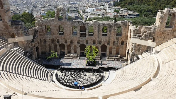 Vue de l'Odéon d'Hérode Atticus à Athènes, un amphithéâtre antique emblématique avec des gradins en pierre, des ruines majestueuses en arrière-plan et une vue sur la ville moderne d'Athènes entourée de collines verdoyantes.